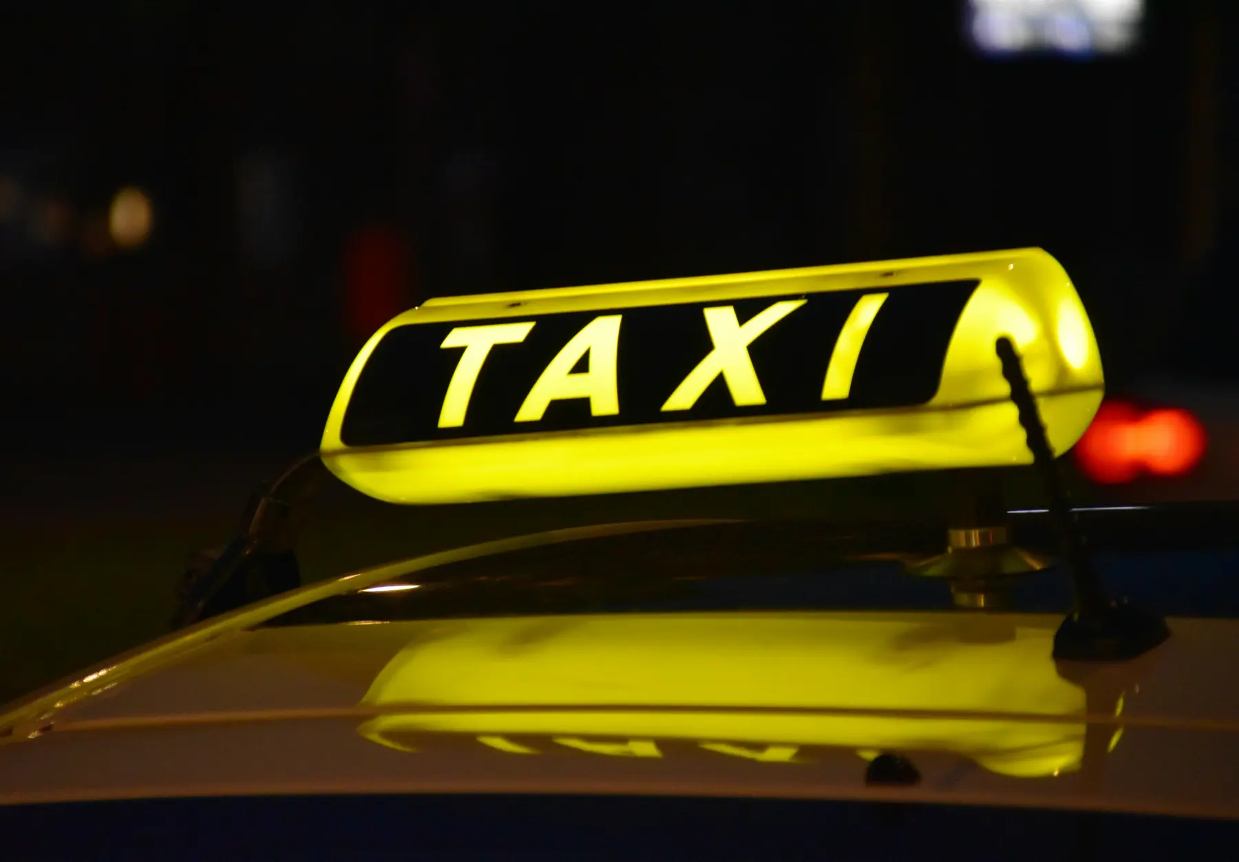 A taxi with its roof sign lit at dusk